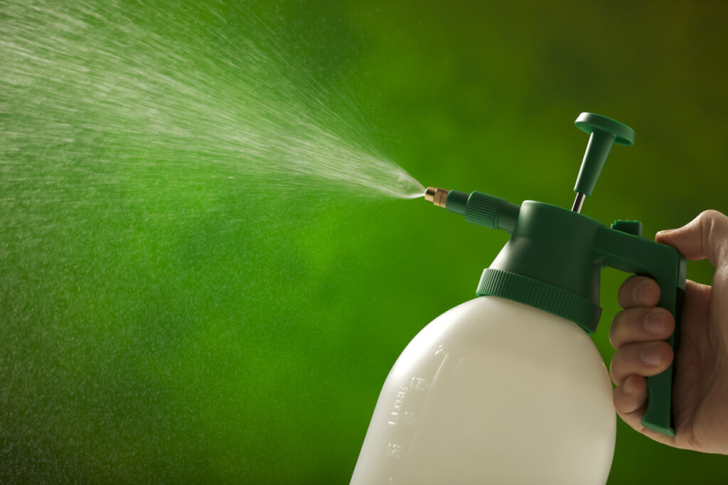 A man is holding a plastic garden spray bottle and spraying water out of the nozzle.
