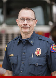 Deputy Chief of Community Outreach and Marketing Rodger Ricciuti standing in front of a fire engine