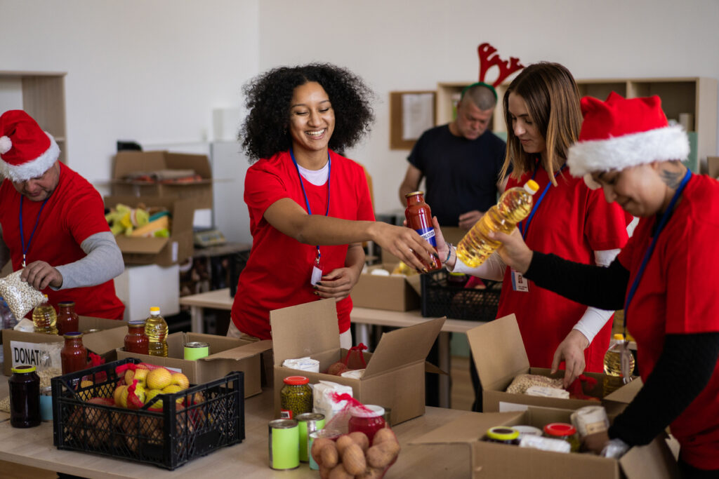 Multi-ethnic charity workers packing donated food into crates in a distribution warehouse, working for homeless and disadvantaged people on a charity drive at Christmas